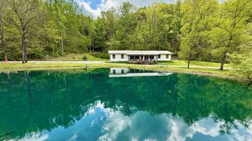 A house with a porch overlooking a clear lake, surrounded by trees.