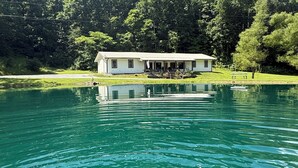 A lakeside cabin with a dock, surrounded by lush greenery and a clear blue sky. - 55 ACRE WATERFRONT RETREAT ~HOT TUB~SWIM ~FISH ~KAYAK ~HIKE ~1 ACRE SPRING POND~ (Columbia)