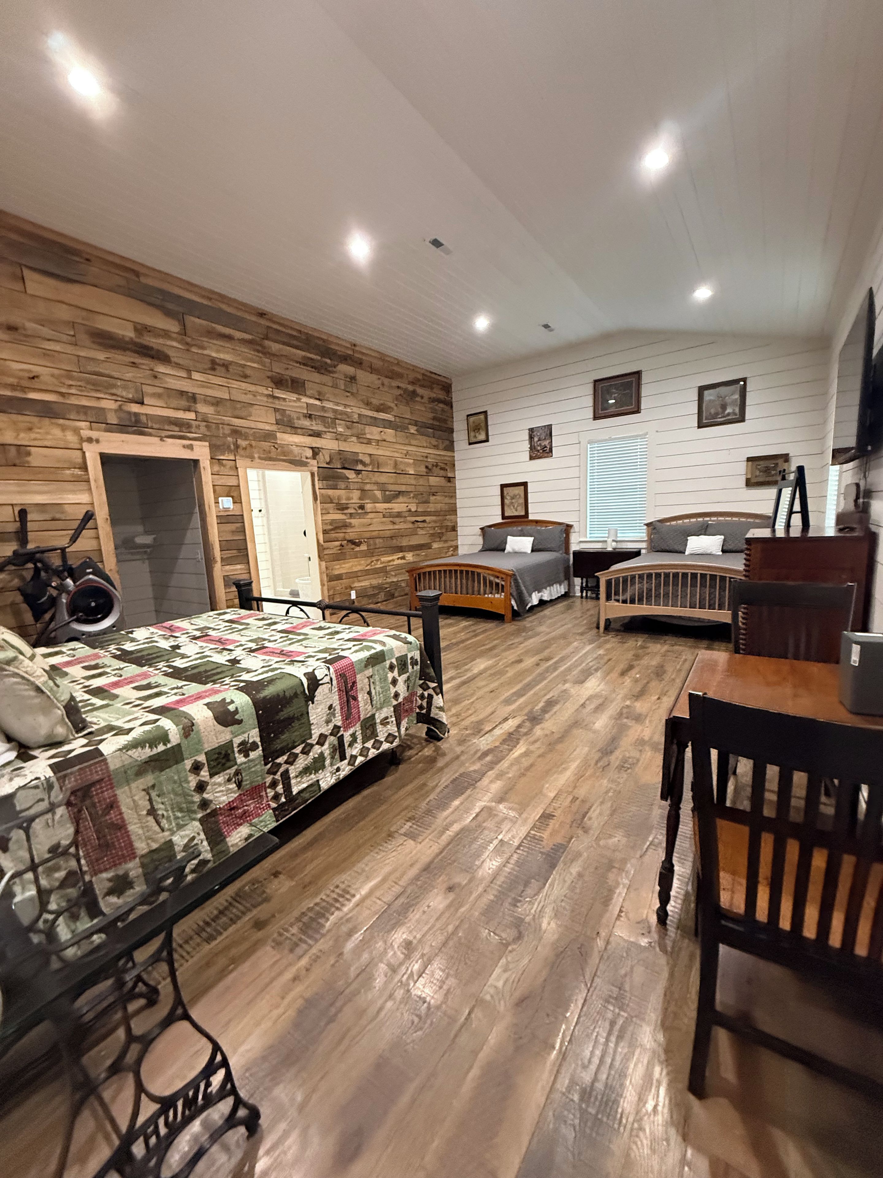 Une pièce avec un plancher en bois, un lit recouvert d’une courtepointe, un bureau avec une chaise et un téléviseur fixé au mur.