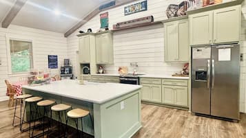 A kitchen with a large island, bar stools, a refrigerator, and a wooden floor.