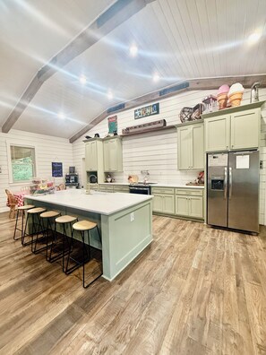 A kitchen with a large island, bar stools, a refrigerator, and a wooden floor. - 55 ACRE PRIVATE WATERFRONT RETREAT~HOTTUB~FISHING~KAYAK~TRAILS~FIRE PIT🔥 (Columbia)