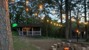 A rustic cabin with a porch, surrounded by trees and a fire pit. - Loblolly Pines Adventure Camp Unit 3 (Eureka Springs)