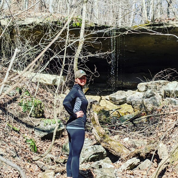 A person standing outdoors near a rocky area with a stream.