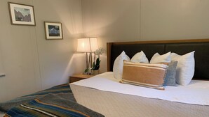 A hotel room with a large bed, a nightstand with a lamp, and two framed pictures on the wall. - Loblolly Pines Adventure Camp Unit 3 (Eureka Springs)
