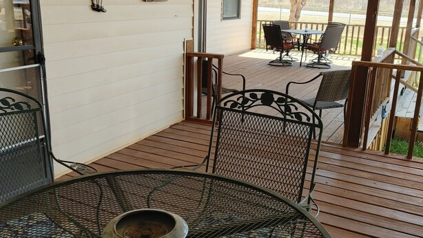 Un patio techado con una mesa y sillas de metal redondas, un letrero de bienvenida y vistas al exterior.