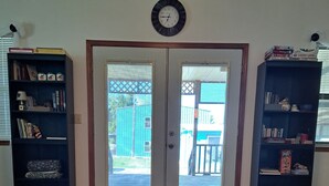 Una habitación con una alfombra estampada, dos estanterías azul oscuro, un reloj en la pared y una puerta que da al exterior.