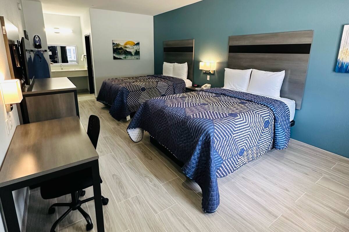 A hotel room with two beds, a desk, and a chair.