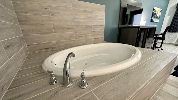 Een moderne badkamer met een vrijstaand bad, een wastafel met spiegel en een aan de muur bevestigde televisie.