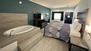 Een moderne hotelkamer met een ruime badkuip, een bed met behang, een televisie en een bureau met een stoel.
