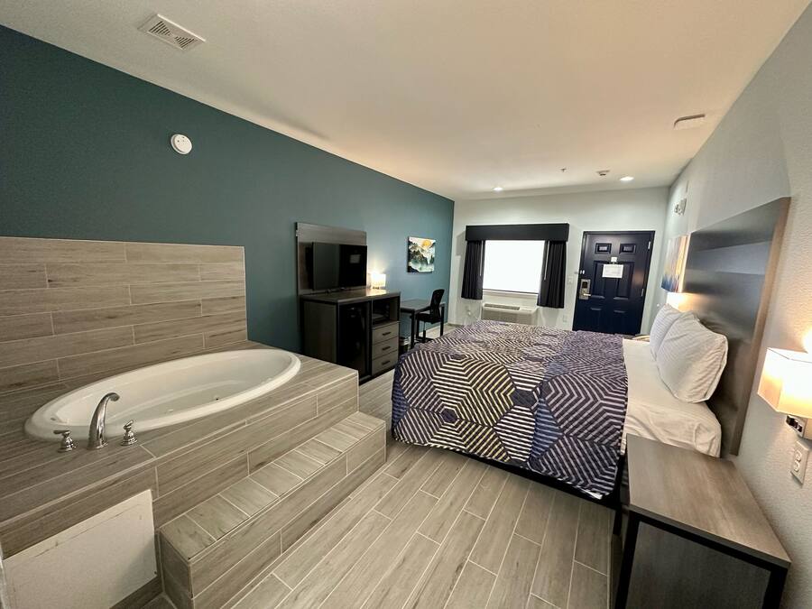 Una habitación de hotel moderna con una bañera grande, una cama con ropa de cama estampada, un televisor y un escritorio con una silla.