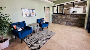Een hal met twee blauwe fauteuils, een klein rond tafeltje, een tapis plat en een potplant.