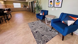 Een ruime woonkamer met een keuken op de achtergrond, een blauwe bank, een klein rond tafeltje en een vloerkleed met dessin.