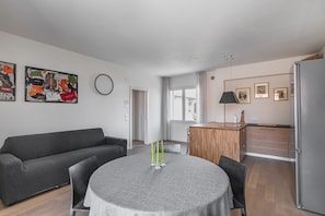 A modern living room with a grey sofa, a round table with candles, and a kitchen area with a fridge.