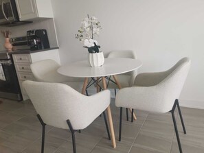 Eine moderne Küche mit weißen Schränken, einer Kaffeemaschine und einem weißen Tisch mit Stühlen.