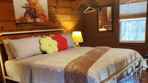 Camera da letto in una baita di legno, con un letto, cuscini, una lampada da comodino e una finestra.
