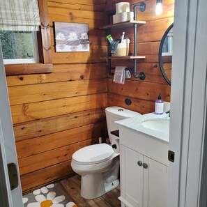 Een kleine badkamer met houten lambrisering, een toilet, wastafel en spiegel.