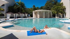 A swimming pool with lounge chairs and a sunbed, surrounded by palm trees and a building with a white facade. - Presidential Suites (Puerto Plata)