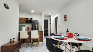 Una cucina compatta con elettrodomestici moderni, una zona pranzo con un tavolo rotondo e sedie, e un piccolo mobile che ospita un oggetto decorativo.