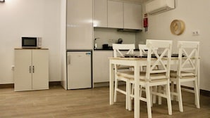 A compact kitchen with white cabinets, a microwave, a refrigerator, and a dining table with four chairs. - Plátanos & River Views I (Ponte de Lima)
