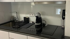 A modern kitchen with white cabinets, a black countertop, a coffee maker, and a wine glass. - Plátanos & River Views I (Ponte de Lima)
