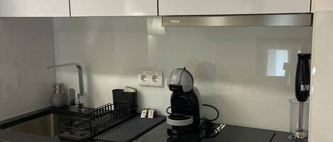 A modern kitchen with white cabinets, a black countertop, a coffee maker, and a wine glass.