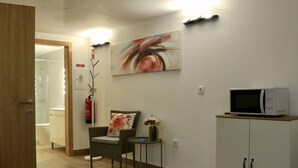 A hotel lobby with a wooden door, a seating area with a chair and table, a wall-mounted painting, a fire extinguisher, a microwave, and a cabinet. - Plátanos & River Views I (Ponte de Lima)