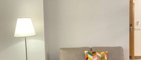 Een moderne woonkamer met een grijze bank, een kleurrijk kussen met een chevrondpatroon, en een vloerlamp.
