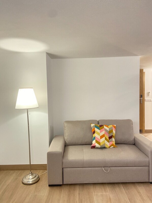 A modern living room with a grey sofa, a colorful chevron-patterned pillow, and a floor lamp.