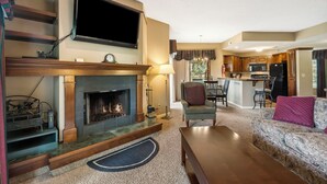 A living room with a fireplace, a television, and a kitchen in the background.