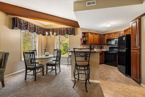 A kitchen with wooden cabinets, a black refrigerator, and a dining area with a table and chairs. - 2 Bedroom Villa at StoneBridge Village (Reeds Spring)