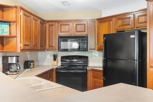 A kitchen with wooden cabinets, a black refrigerator, a microwave, a stove, and a coffee maker.