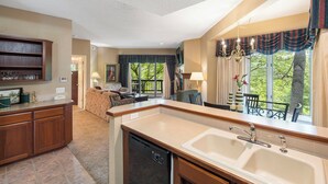 A kitchen with a dishwasher, a dining area with a table and chairs, and a living room with a sofa and a window with curtains. - Two Bedroom Villa in a Gorgeous, Gated Community near Silver Dollar City (Reeds Spring)