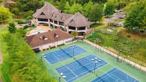 Ein Tennisplatzkomplex mit mehreren Plätzen, einem Gebäude mit markanter Dachform und umliegender Grünfläche.