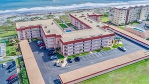 A coastal hotel with multiple buildings, a parking area, and a view of the ocean. - Cozy Ground Floor Walkout w/Ocean View (Cocoa Beach)