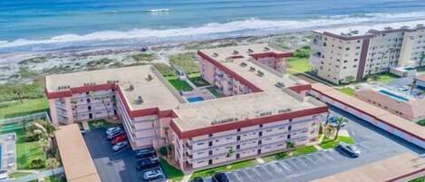A coastal hotel with multiple buildings, a parking area, and a view of the ocean.
