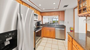 A modern kitchen with wooden cabinets, stainless steel appliances, and a tiled floor. - Cozy Ground Floor Walkout w/Ocean View (Cocoa Beach)