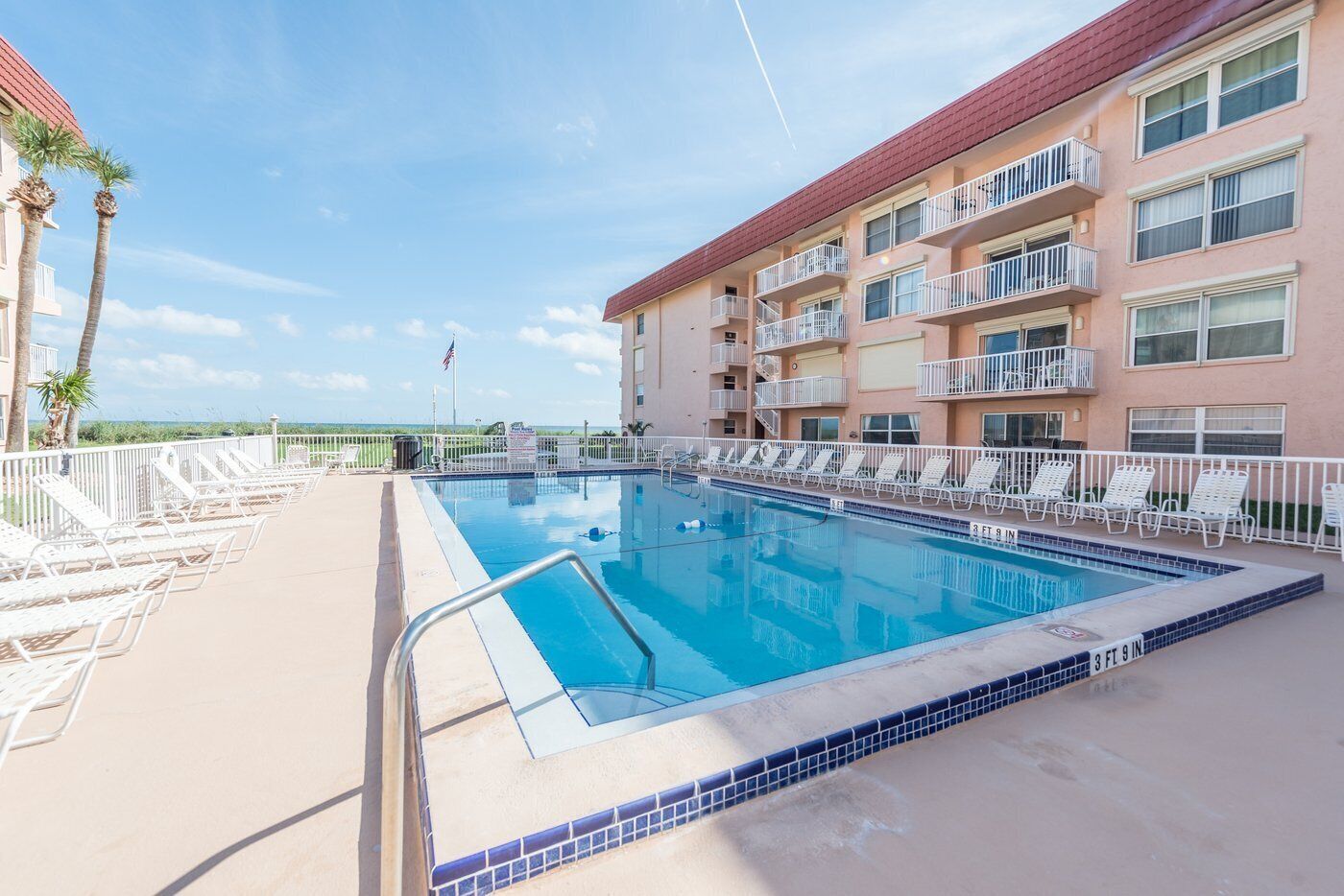 A swimming pool with lounge chairs and a building with balconies.