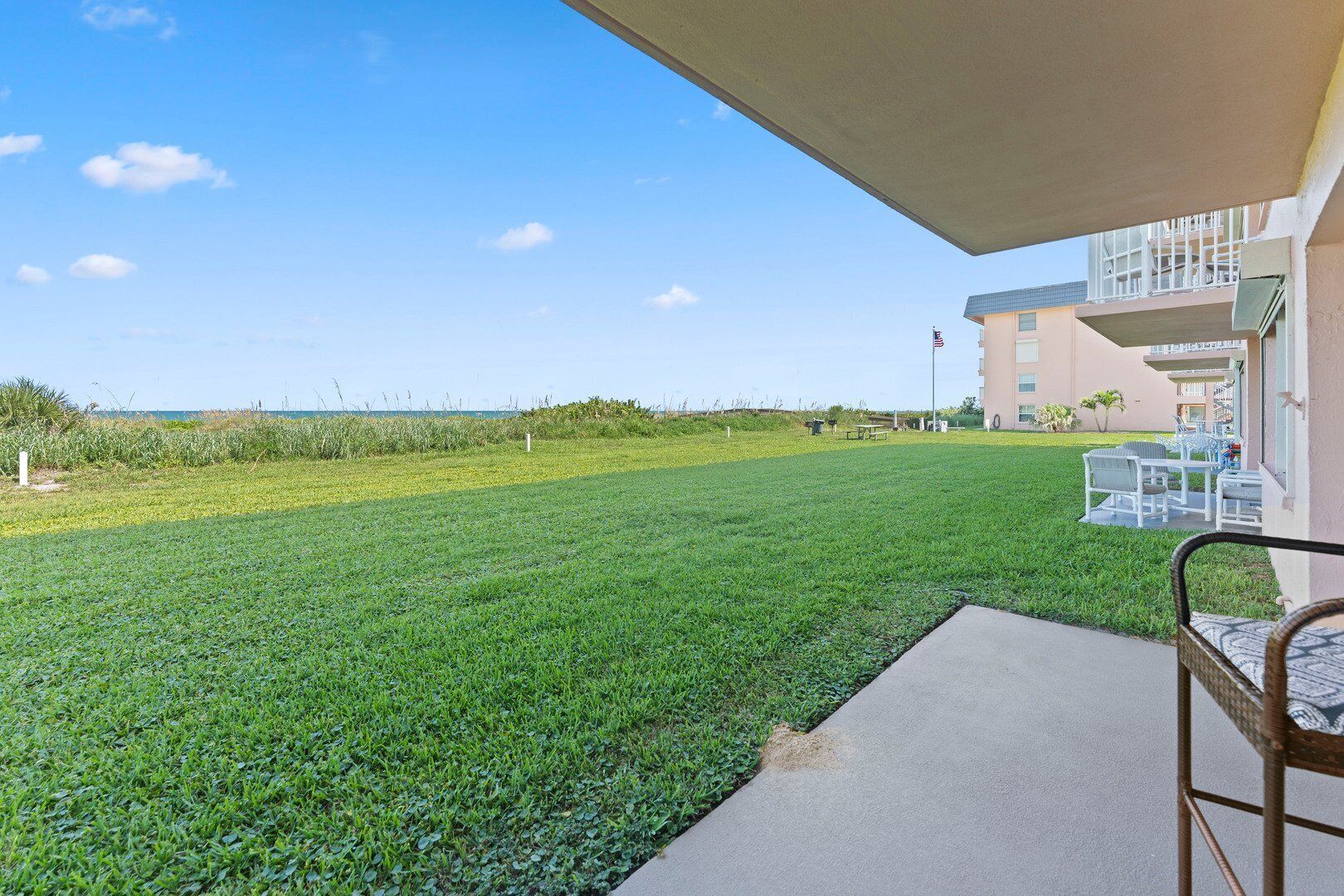 A grassy patio area with a view of the ocean, a building with a balcony, and outdoor furniture.