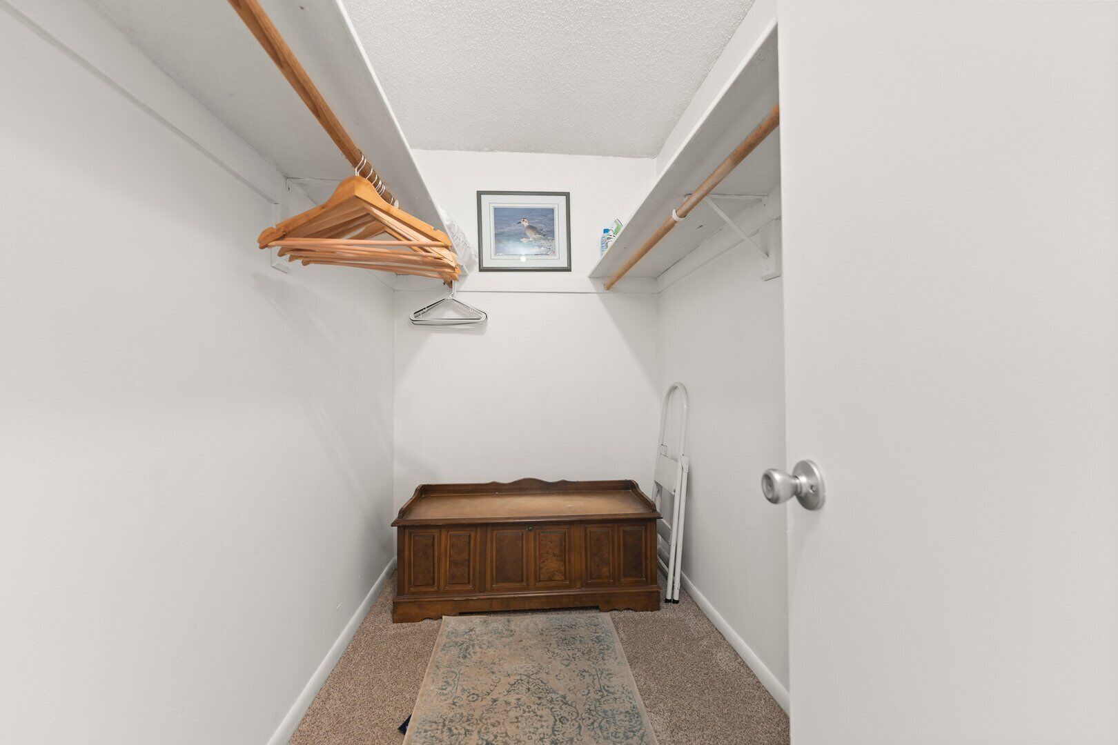A narrow hallway with a wooden bench, a hanging clothes rack, a framed picture on the wall, and a radiator.