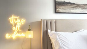 A neatly made bed with white linens and a headboard, a bedside table with a lamp, and a neon sign on the wall. - Cozy 2/1 Close to Theme Parks! (St. Cloud)