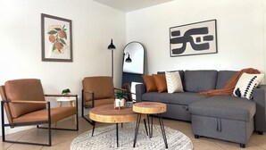 A modern living room with a grey sofa, brown armchair, and a round wooden coffee table. - Cozy 2/1 Close to Theme Parks! (St. Cloud)