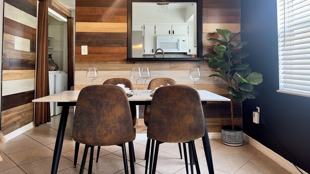 A dining area with a wooden wall panel, a hanging light fixture, a mirror, and a potted plant. - Cozy 2/1 Close to Theme Parks! (St. Cloud)