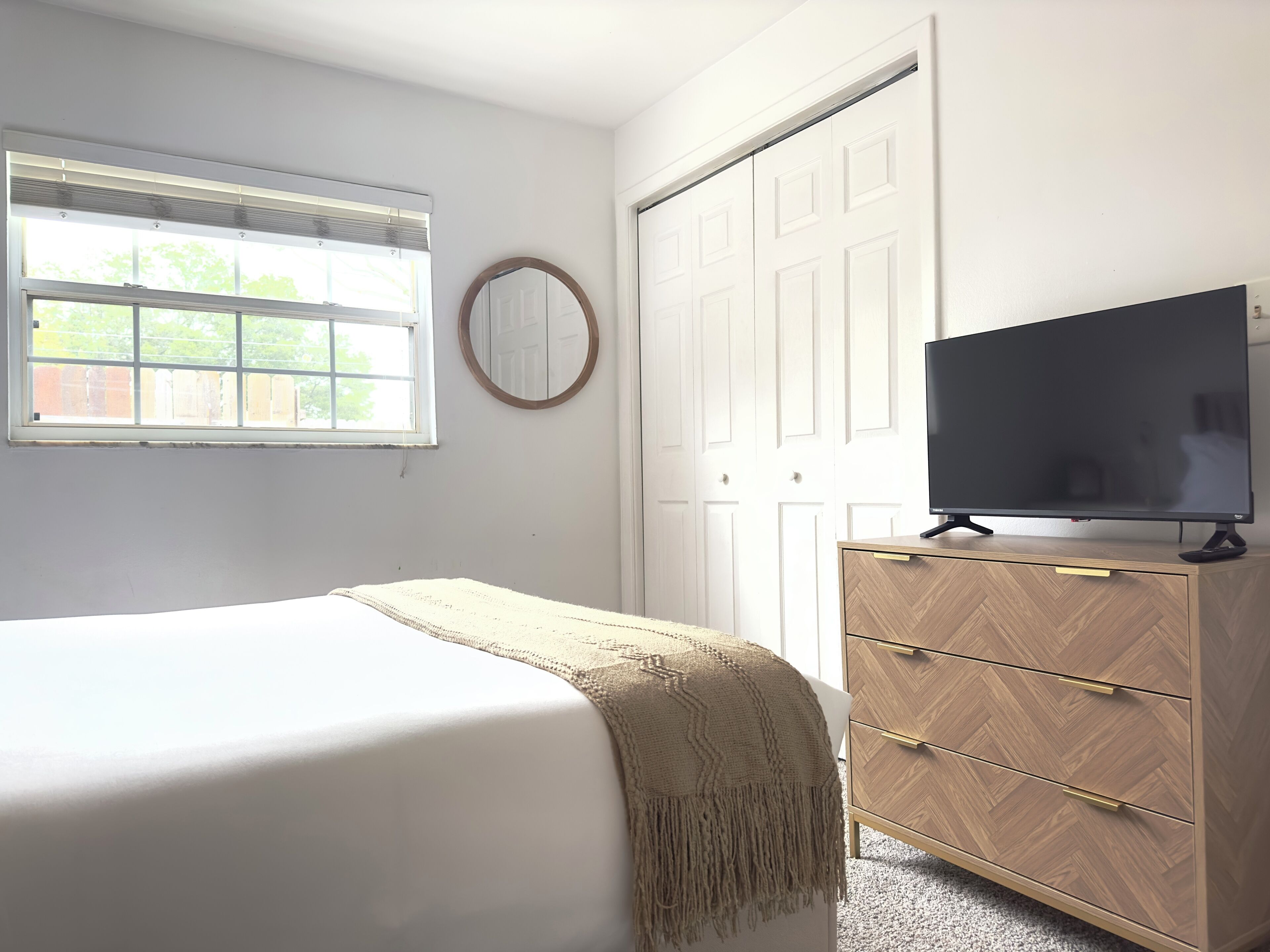 Een slaapkamer met een bed, een dressoir, een televisie, een raam en een deur.
