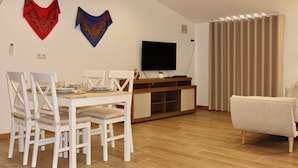 A dining area with a table and chairs, a television on a stand, and a window with curtains. - Plátanos & River Views III (Ponte de Lima)