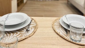 A dining table set with plates, cutlery, and glasses, with a TV and a lamp in the background. - Plátanos & River Views III (Ponte de Lima)