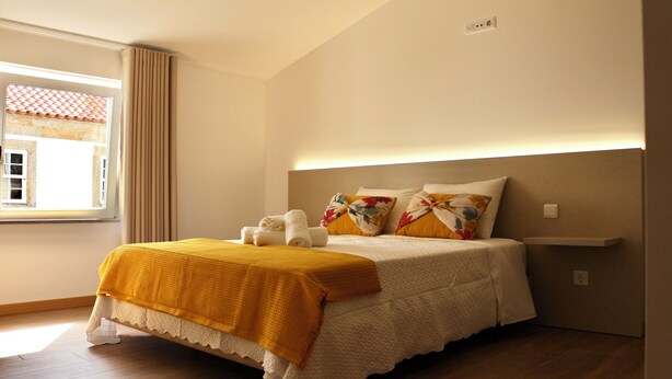 A neatly made bed with a yellow blanket, white pillows, and a headboard with built-in lighting. - Plátanos & River Views III (Ponte de Lima)