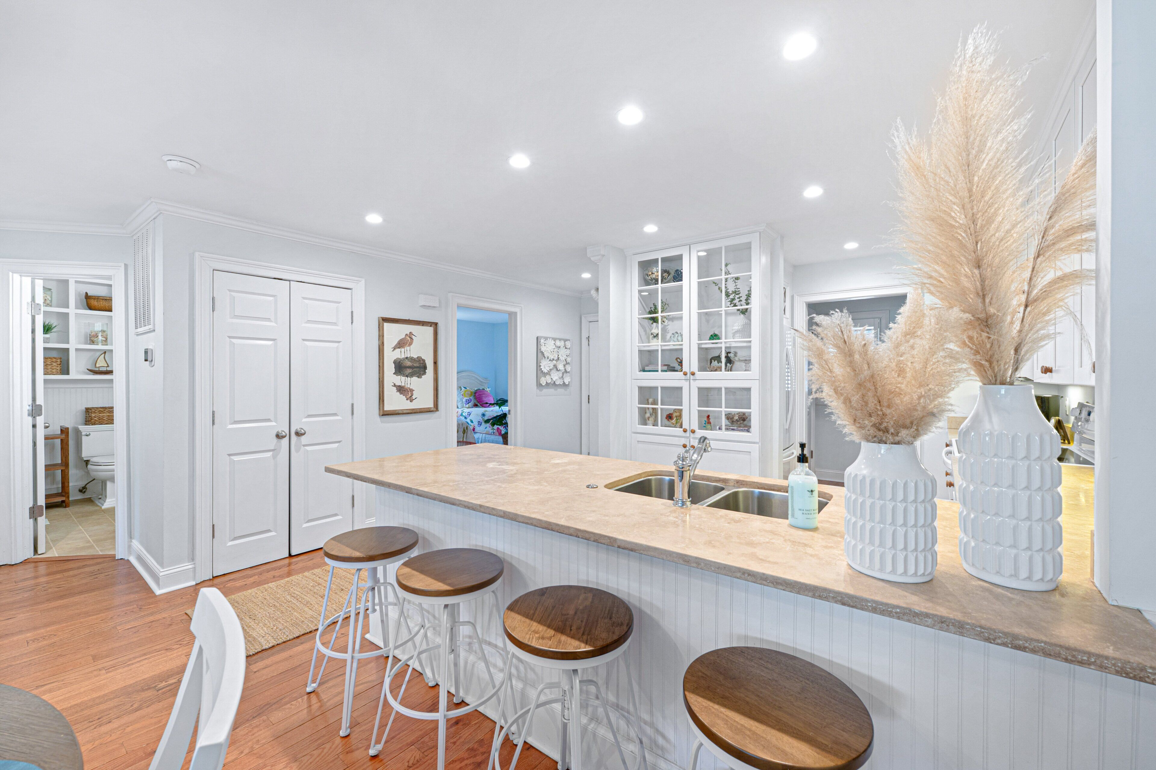 A kitchen with white cabinetry, a central island with stools, and a sink.