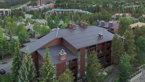 A multi-story building with a sloped roof, surrounded by trees and a mountainous backdrop.