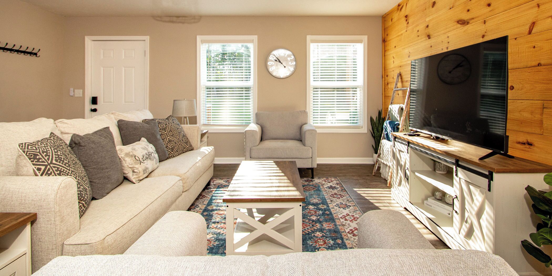 A living room with a sofa, armchair, coffee table, TV, and wooden wall paneling.