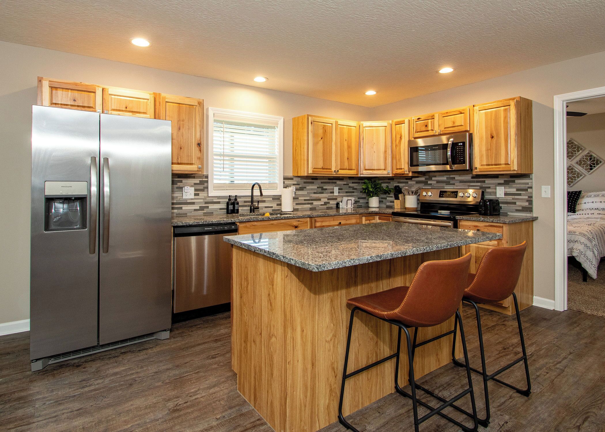 A modern kitchen with wooden cabinets, stainless steel appliances, a granite countertop, and a bar stool.